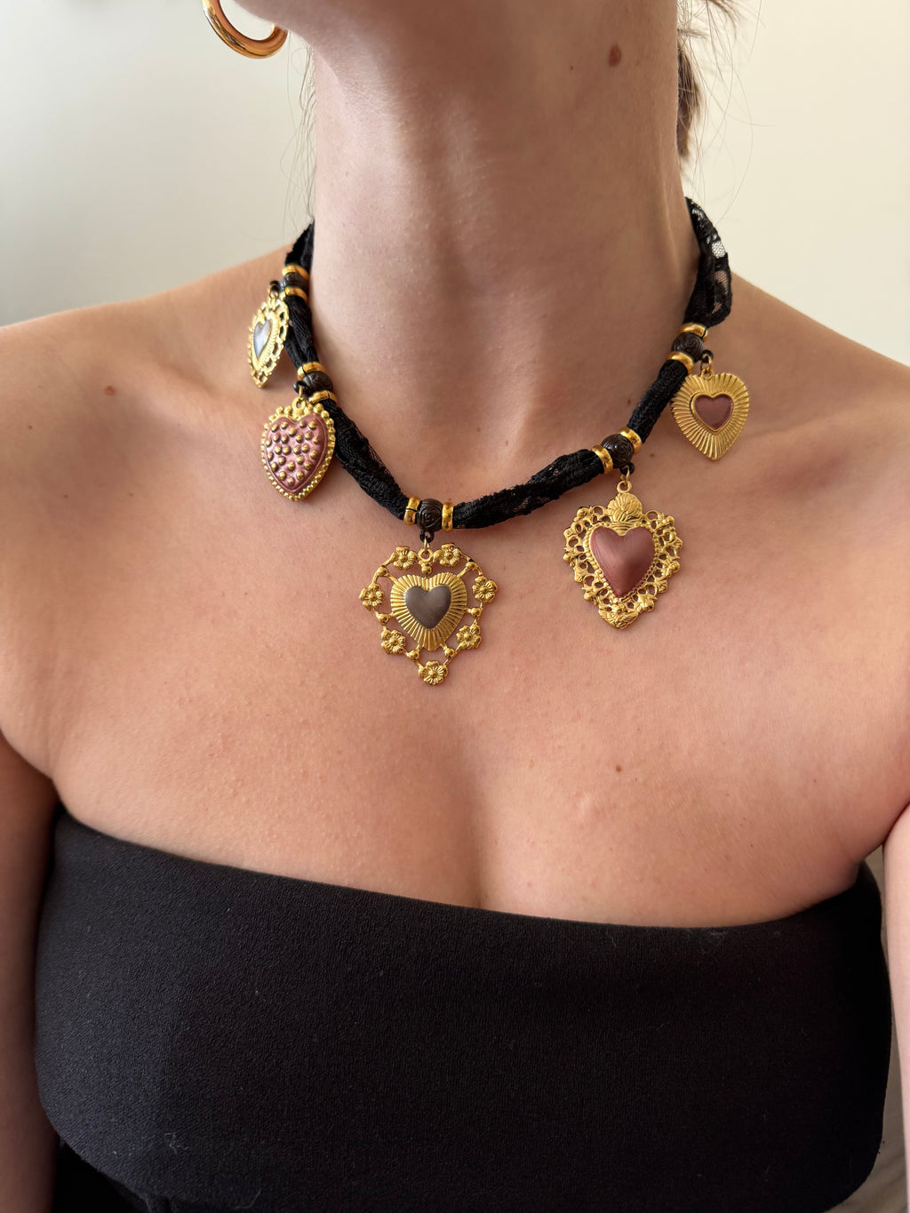 Close-up of a person's arm wearing gold and black bracelets with heart and leaf designs.